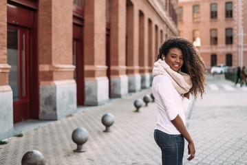 Portrait of cheerful young lady out on the city street listening to music with earphones.