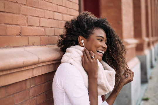 Young beautiful afro woman outdoor in city street listening music with headphones.