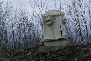The sagging head of the ventilation shaft of an old abandoned bomb shelter in a gloomy landscape