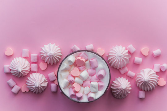 Top view hot beverage with whipped cream,marshmallows and heart shaped chocolate candies on pink pastel  background