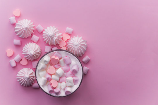 Top view hot beverage with whipped cream,marshmallows and heart shaped chocolate candies on pink pastel  background