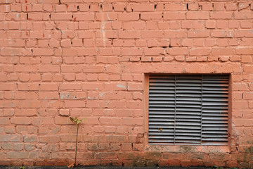 Fototapeta na wymiar The wall is made of bricks. It is painted with orange paint. Background. Exterior. Technological window with a lattice. Dampness at the bottom of the wall