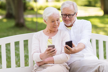 happy senior couple with smartphones at park