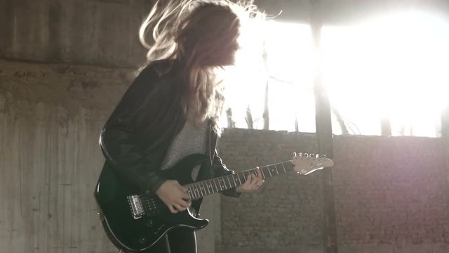 Sexy Excited joyful young woman guitarist musician in black leather jacket with electric guitar playing hard rock music shouting and shaking head jumping. Entertainment and musical concept.