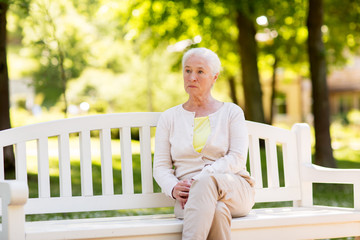 sad senior woman sitting on bench at summer park