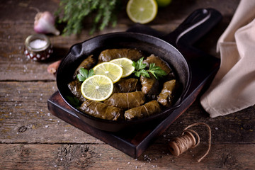 Dolma, stuffed grape leaves with rice and beef minced meat in a cast-iron frying pan on an old wooden background. Middle Eastern cuisine.