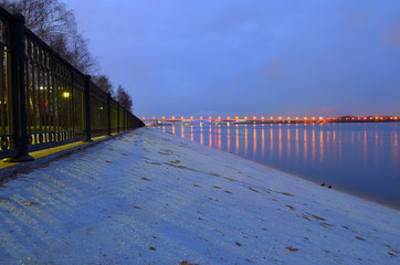 Night city embankment in Perm and bridge through the Kama river, lit by lanterns, the reflection of light in water.