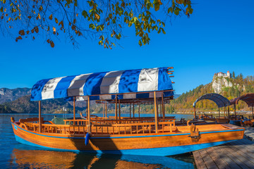 Bled, Slovenia - Traditional blue Pletna boat in the autumn sunshine at Lake Bled with Bled Castle at background