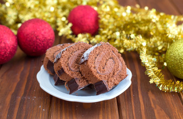 Christmas chocolate roll on a wooden table with red and gold balls Christmas toys