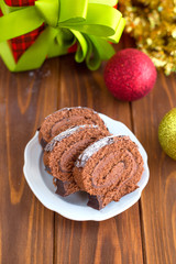 Christmas chocolate roll on a wooden table with red and gold balls Christmas toys