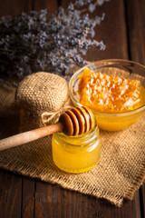 Honey dripping from a wooden honey dipper in a jar on wooden grey rustic background