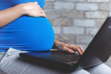 Pregnant woman in blue wear using a laptop and working at home. Crop. Copy space.