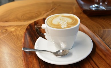 Cup of foamy cappuccino on a plate on a wooden table.
