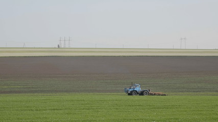 Blue wheeled tractor plowing a green field