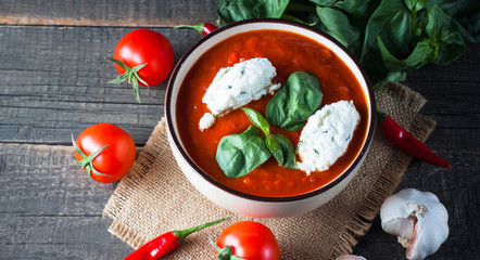 Chili tomato soup with sour cream sauce, cottage cheese, basil and red hot peppers on wooden background. Healthy, vegan and dieting lunch and dinner concept.