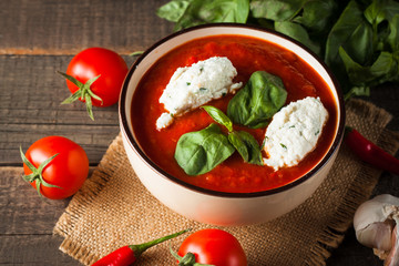 Chili tomato soup with sour cream sauce, cottage cheese, basil and red hot peppers on wooden background. Healthy, vegan and dieting lunch and dinner concept.