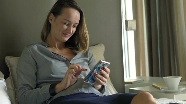 Young businesswoman texting on smartphone lying on bed in hotel room 
