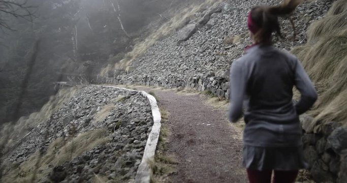 Athlete girl running through snowy trail path.Following behind.Real people woman runner sport training in autumn or winter in wild mountain outdoors nature, bad foggy weather.4k 60p slow motion video