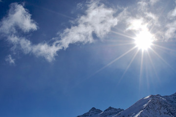 the sun shines through the clouds. the snow lies on the mountain peaks.