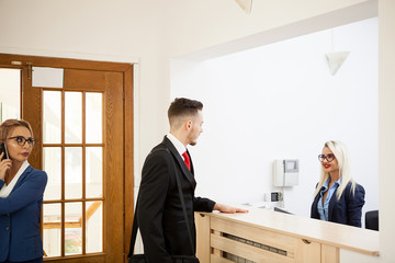 Busy businessman in office reception area talking with secretary