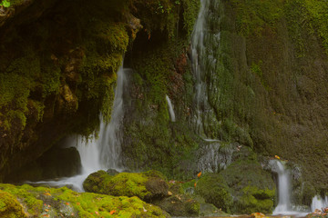 Fototapeta na wymiar Smoll waterfall among rocks covered with green moss