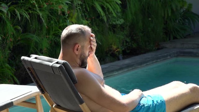 Man lying on sunbed and looks very worried, steadycam shot, slow motion shot at 240fps
