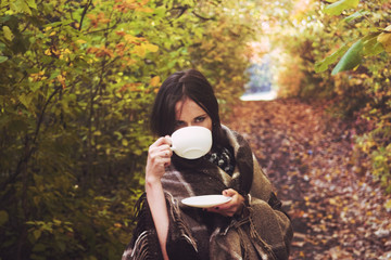 The girl brunette in autumn forest drinking hot coffee at dawn