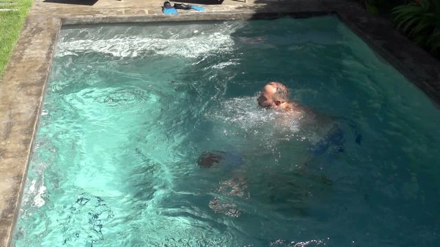 Boy diving in the swimming pool and father helps him, steadycam shot, slow motion shot at 240fps
