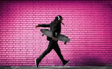 Handsome young dreadlocks skater with headphones running in a suit near the pink wall on the street. © Dusan Petkovic