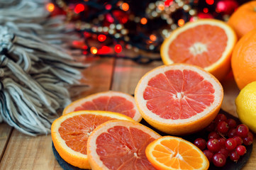 Citrus fruits on wooden table with woolen blanket and red christmas lights. Grapefruit, orange,...