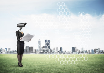 Camera headed woman standing on green grass against modern citys