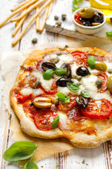 Homemade pizza with tomatoes, olives, salami, mozzarella cheese and fresh basil on a wooden rustic table