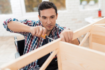 The young man in wheelchair tries himself to fold his bookcase.