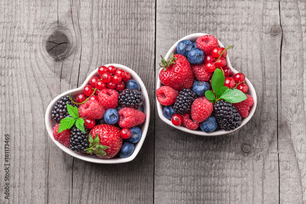 Wall mural Berries overhead mix with leaves colorful closeup assorted in two heart shaped ceramic jars. Raspberry, blueberry, red currant, strawberry on rustic wooden table in studio.