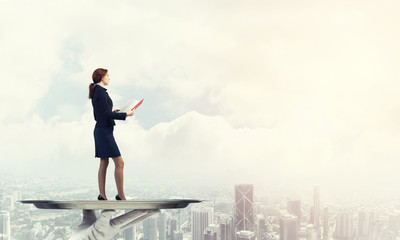 Obraz premium Attractive businesswoman on metal tray with red book in hands against cityscape background