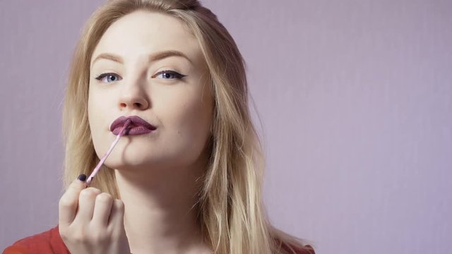 Beautiful girl paint her lips with purple lip gloss