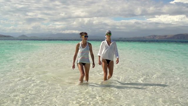 Women walking in the clear sea and waving to the camera, steadycam shot, slow motion shot at 240fps
