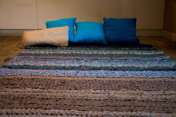 brown turquoise hand-woven carpet lying on a wooden floor with comfortable blue pillows in the background