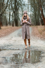 girl in a knitted hat and scarf at a puddle in the fall on nature.