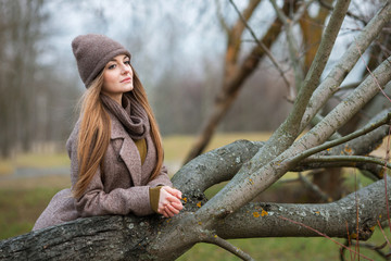 girl in a knitted hat and scarf in a fallen tree in the fall on the nature.