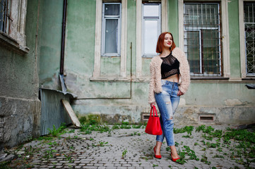 Red haired girl with red handbag posed at street of city.