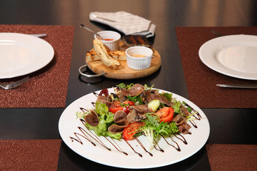 Salad with beef tongue with vegetables and herbs, dressed with sauce on a white plate.