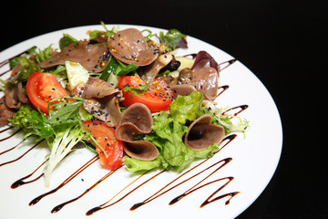 Salad with beef tongue with vegetables and herbs, dressed with sauce on a white plate.