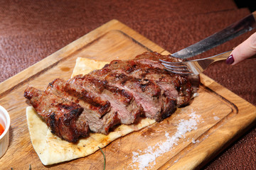 Medium-roasted steak cut into pieces on a wooden board with sauce and seasonings.