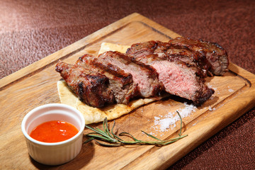 Medium-roasted steak cut into pieces on a wooden board with sauce and seasonings.