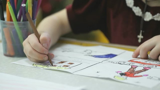 Close-up of unknown little child draws and paints pictures with felt-tip sitting at desk in the kindergarten