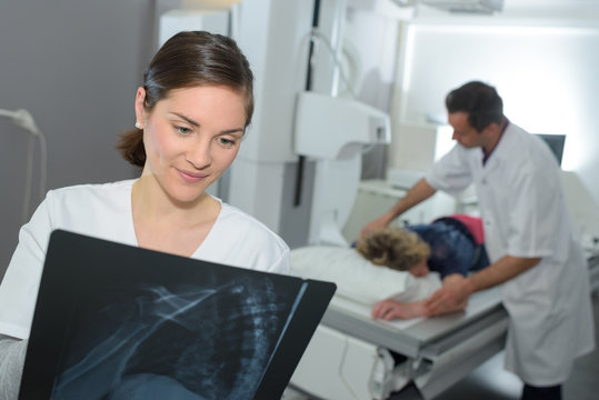 female doctor looking at x-ray with patient and assistant behind