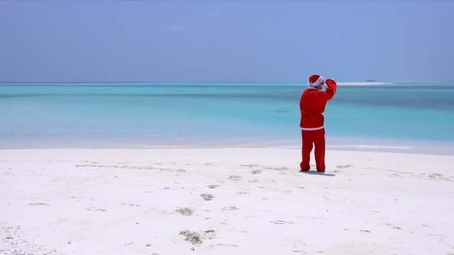 Man in Santa Claus Hat dancing on sandy beach. Christmas vacation on Maldivian islands