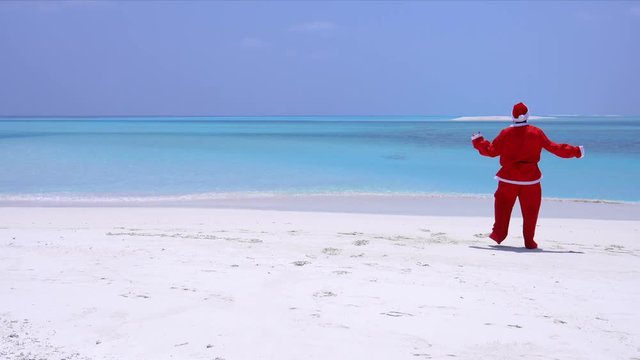 Man in Santa Claus Hat dancing on sandy beach. Christmas vacation on Maldivian islands