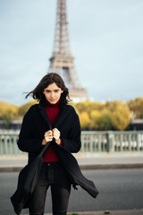 Elegant woman in black coat standing in a park with Eiffel Tower on the background, Outdoor fashion look in Paris